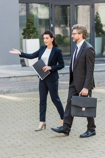 attractive diplomat pointing with hand while walking with man in glasses 