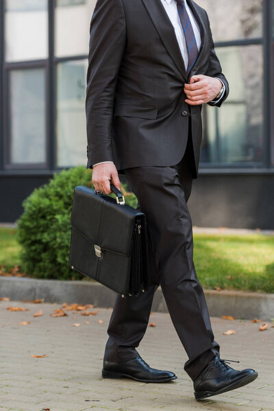 cropped view of diplomat touching blazer while walking with briefcase 