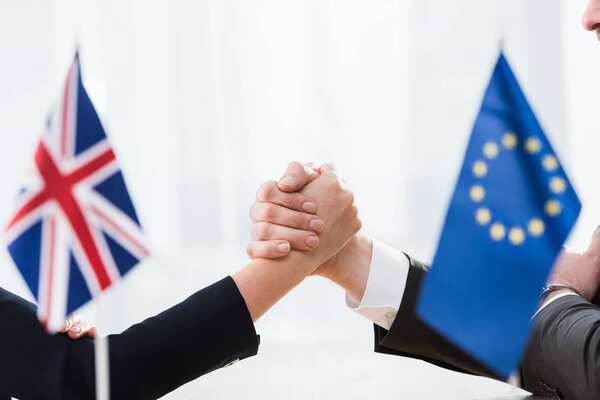 cropped view of ambassadors holding hands near european union and united kingdom flags 