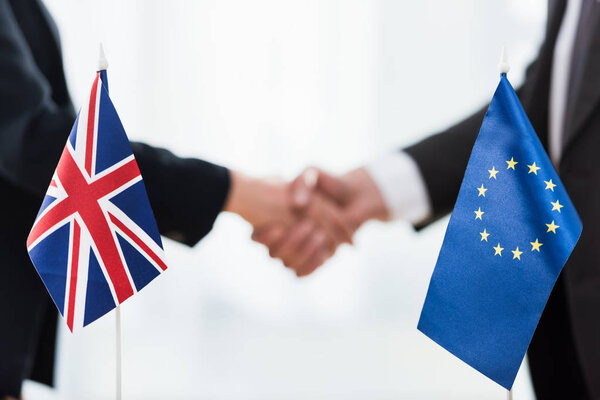 cropped view of ambassadors shaking hands near european union and united kingdom flags 