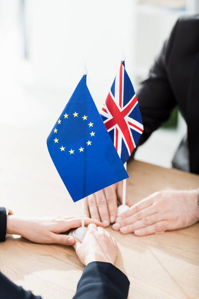 cropped view of ambassadors touching european union and united kingdom flags on table 