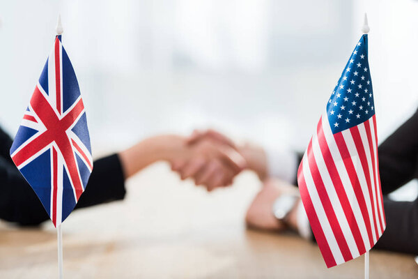 selective focus of flags of usa and united kingdom near diplomats shaking hands