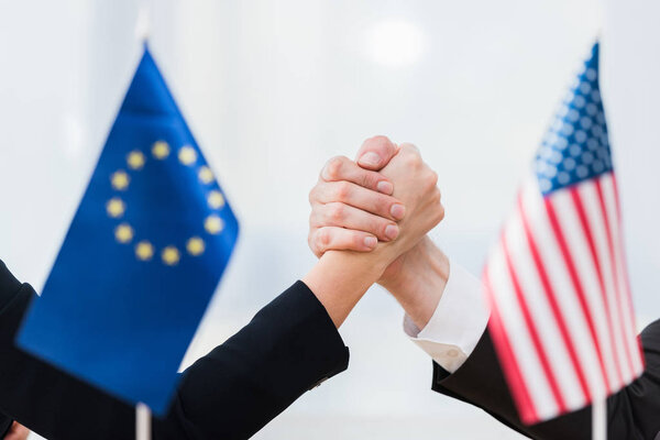 избирательный фокус дипломатов, держащихся за руки возле флагов США и Европейского союза
