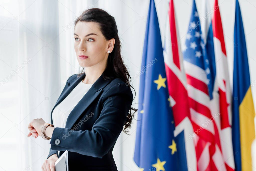 attractive diplomat waiting near flags in embassy 