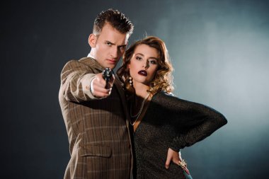 selective focus of dangerous gangster holding gun and standing near attractive woman  on black  clipart