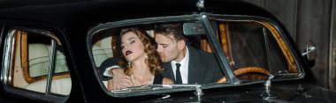 panoramic shot of gangster sitting in retro car with woman  clipart