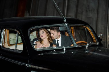 handsome gangster sitting in retro car with woman  clipart