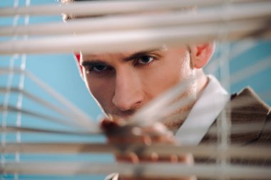 selective focus of dangerous man touching white window blinds  clipart