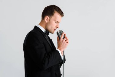 Yakışıklı şarkıcı beyaz üzerinde izole edilmiş retro mikrofona dokunuyor 