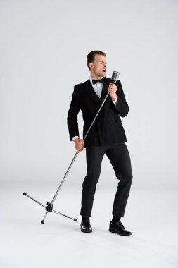 Beyaz mikrofona dokunurken şarkı söyleyen yakışıklı bir adam. 