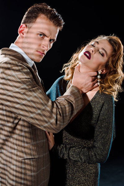 serious gangster touching neck of attractive woman isolated on black 