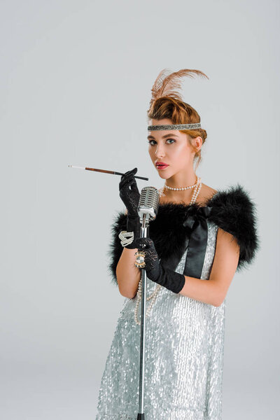 attractive woman with cigarette holder near retro microphone isolated on grey 