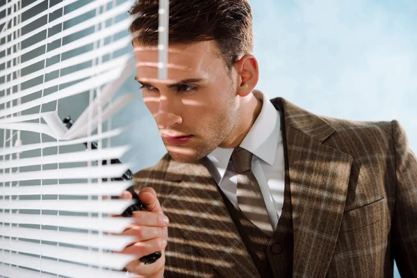 白い銃で窓のブラインドに触れる危険な男の選択的な焦点 — ストック写真