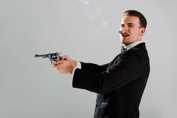 handsome and dangerous man holding gun while smoking isolated on grey 