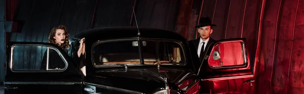 レトロな車の近くに立つ魅力的な女性とハンサムなギャングのパノラマのショット — ストック写真