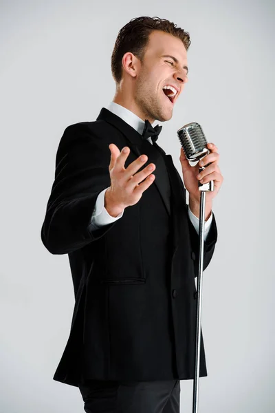 Gri Renkte Izole Edilmiş Mikrofona Dokunurken Şarkı Söyleyen Yakışıklı Adam — Stok fotoğraf