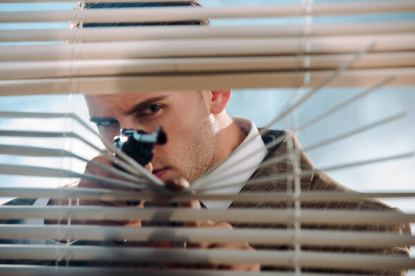 selective focus of dangerous gangster holding gun near window blinds