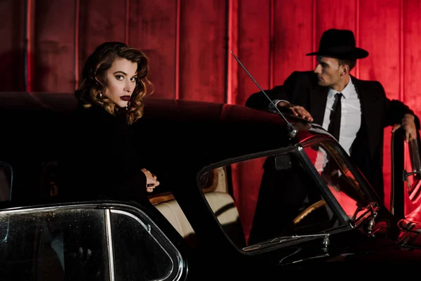 レトロな車や帽子の男の近くに立つ魅力的な女性の選択的な焦点 — ストック写真