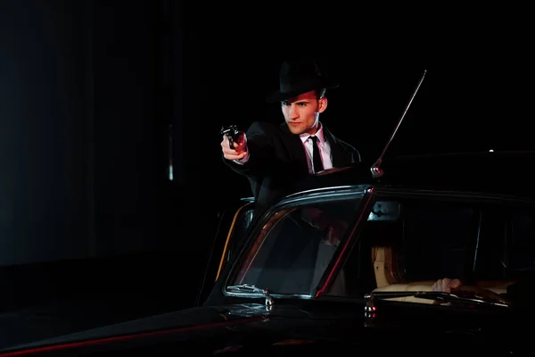 コートを着た武装した男とレトロな車の近くに銃を持った帽子 — ストック写真
