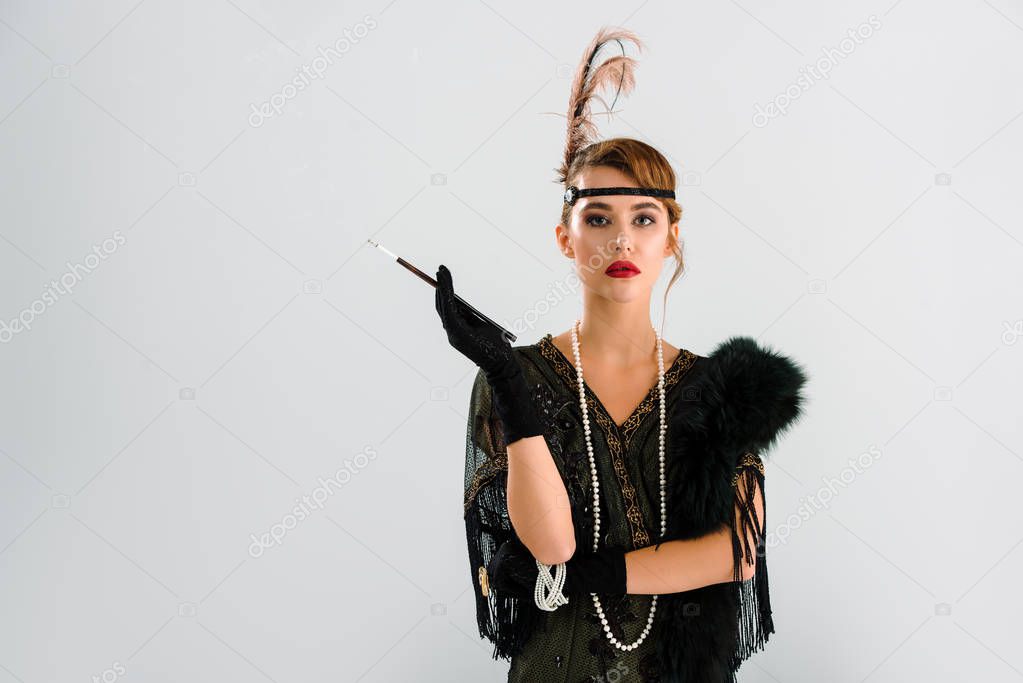 stylish woman with cigarette holder looking at camera isolated on grey 