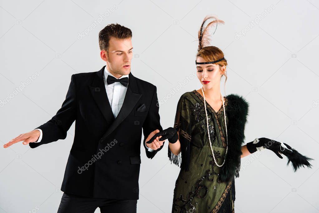 handsome man in suit and attractive woman holding hands and dancing isolated on white