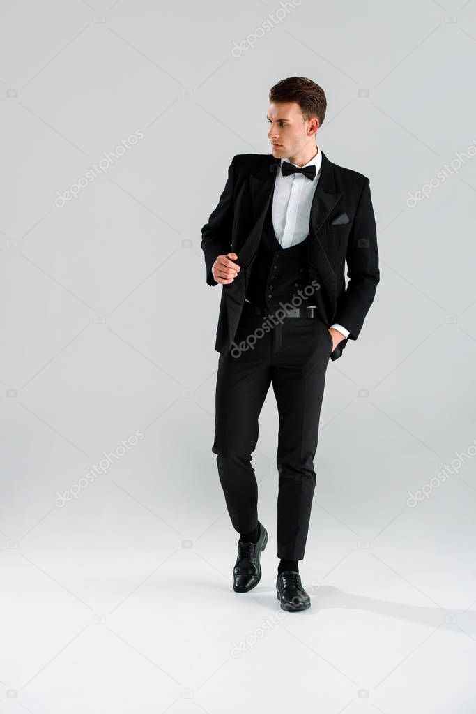 stylish man in suit and bow tie standing with hand in pocket on grey 