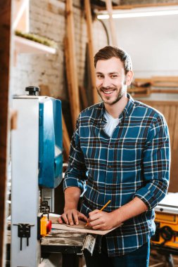 selective focus of happy carpenter holding pencil in workshop  clipart