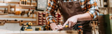 panoramic shot of carpenter holding chisel while carving wood in workshop  clipart