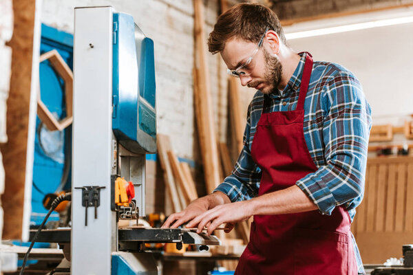selective focus of handsome carpenter in protective glasses using electric woodworking