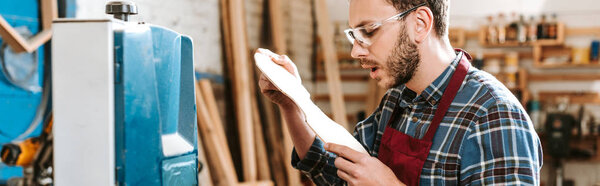 panoramic shot of surprised carpenter looking at wooden cutting board 