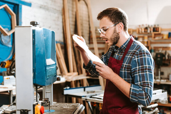 selective focus of surprised carpenter looking at wooden cutting board 