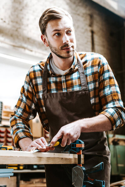 handsome carpenter holding chisel while carving wood in workshop 