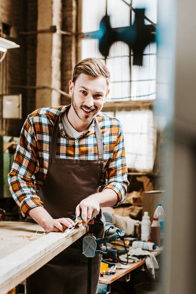 selective focus of cheerful woodworker holding chisel while carving wood in workshop 