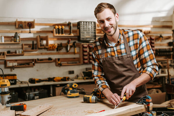 happy bearded carpenter carving wood in workshop 