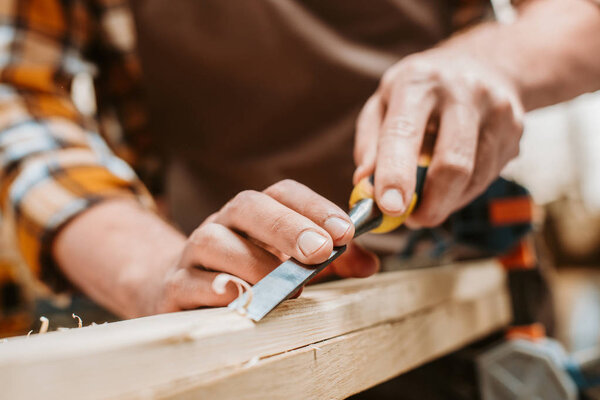 cropped view of carpenter carving wood on workshop 