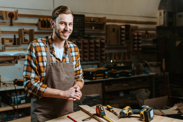 happy woodworker with clenched hands standing near table with tools 