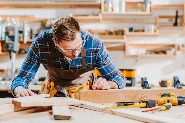 selective focus of woodworker in goggles touching wooden dowel 
