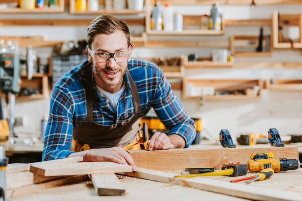 selective focus of happy carpenter in goggles touching wooden dowel 