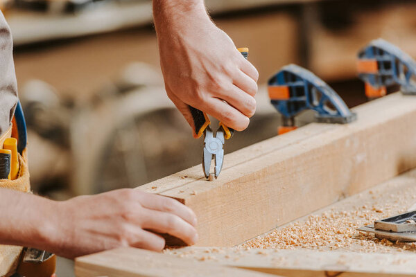 cropped view of carpenter holding pliers near wooden dowel 