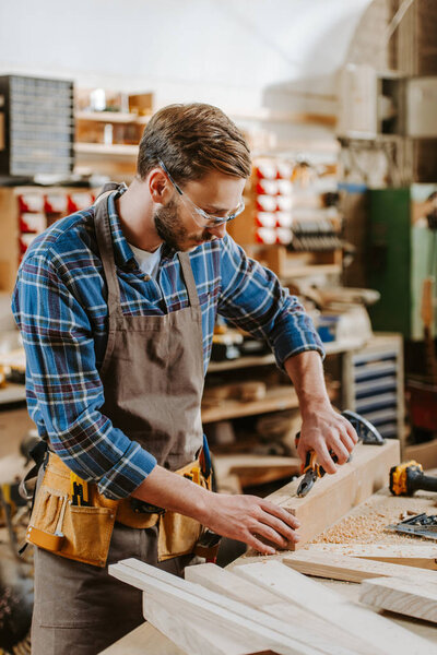 selective focus of carpenter in goggles holding pliers near wooden dowel 