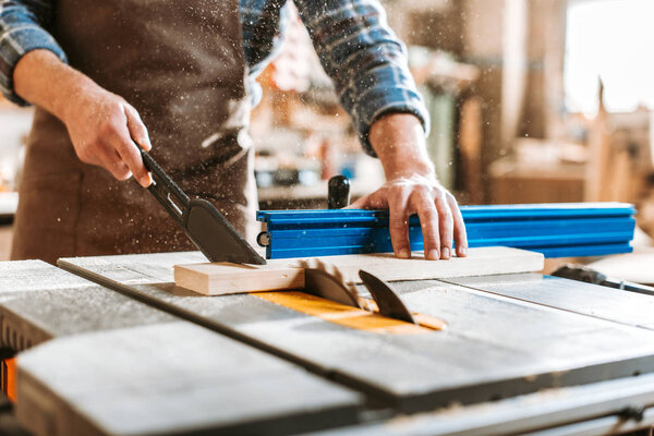 selective focus of woodworker holding plank near circular saw