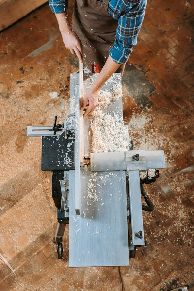 top view of woodworker holding plank near circular saw in carpentry shop 