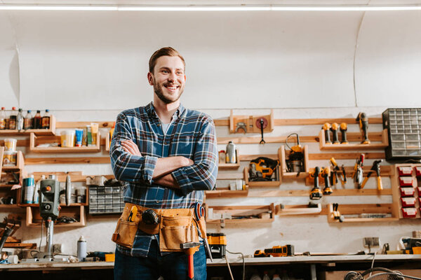 cheerful carpenter in apron standing with crossed arms 