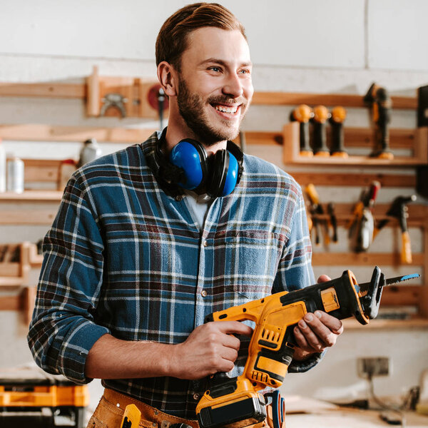 happy bearded carpenter holding hammer drill 