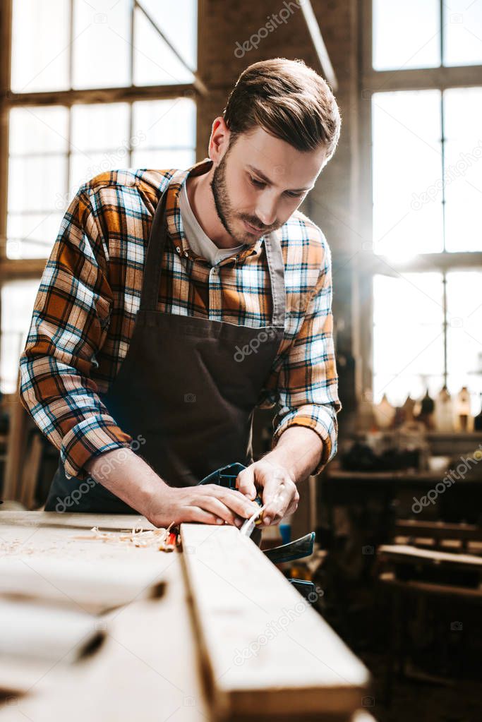 selective focus of bearded carpenter carving wood in workshop 