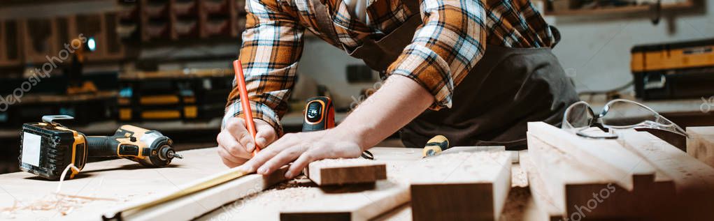 panoramic shot of woodworker measuring wooden plank 