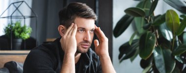 panoramic shot of handsome man with headache touching head in apartment  clipart