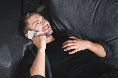 high angle view of handsome man having heart attack and talking on smartphone in apartment  clipart