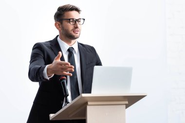 Takım elbiseli işadamı kürsüde dikiliyor ve konferans sırasında konuşuyor.
