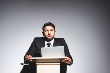 low angle view of scared businessman in suit standing at podium tribune and looking away during conference on white background  clipart